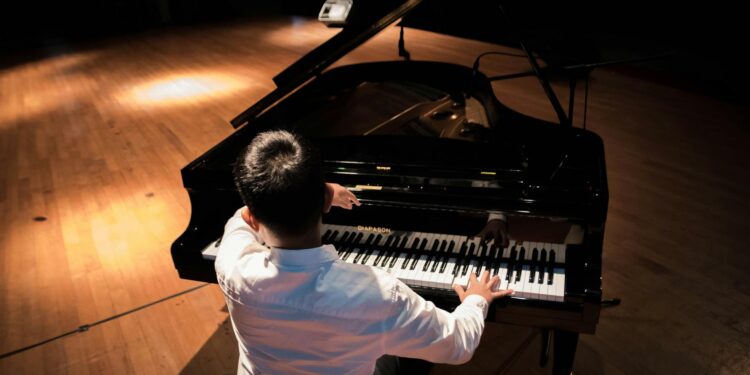 back view photo of a man playing a black grand piano